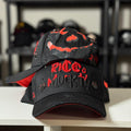 Black and red cap with 'Rico Muerto' text on a white surface